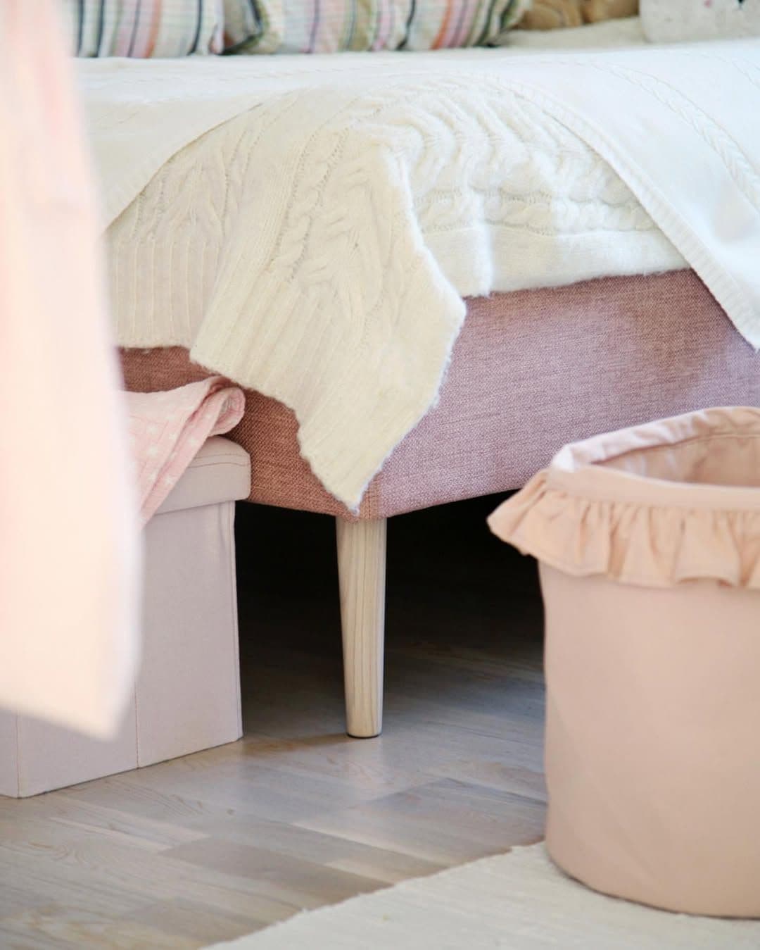 IKEA bed with light wood legs in a soft feminine bedroom with layered textiles