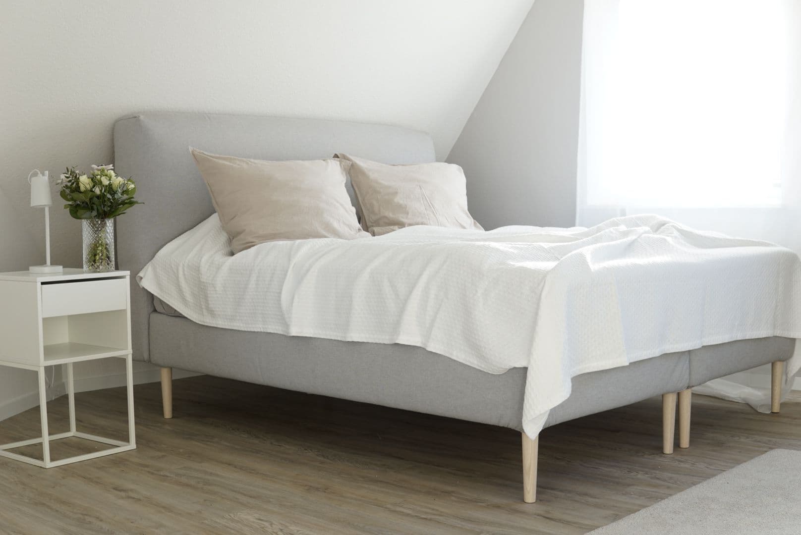 Scandinavian IKEA bed with light wood legs in a calm and minimal bedroom