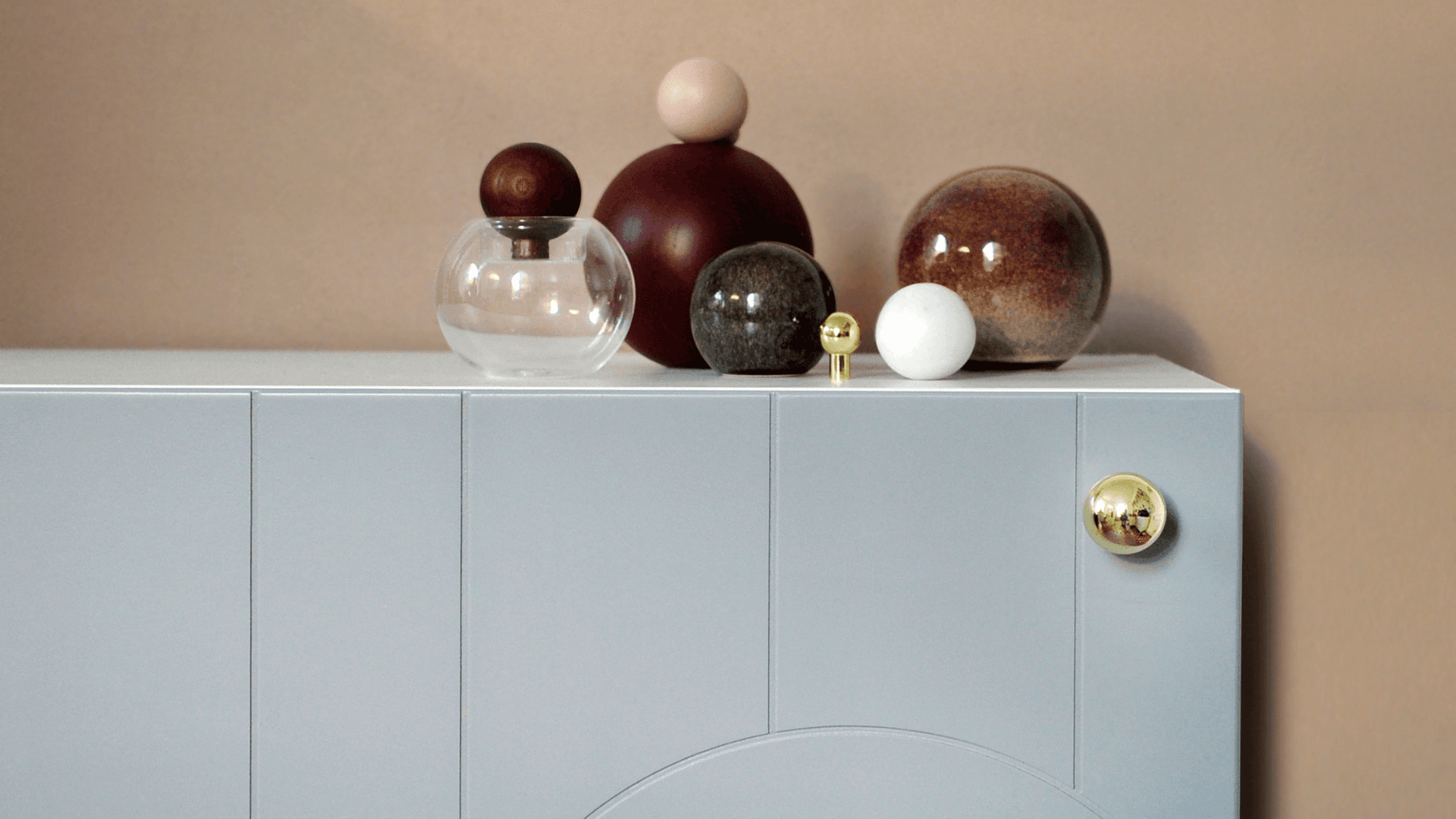 Grey cabinet featuring Prettypegs brass ball knobs styled with decorative round vases in warm tones.